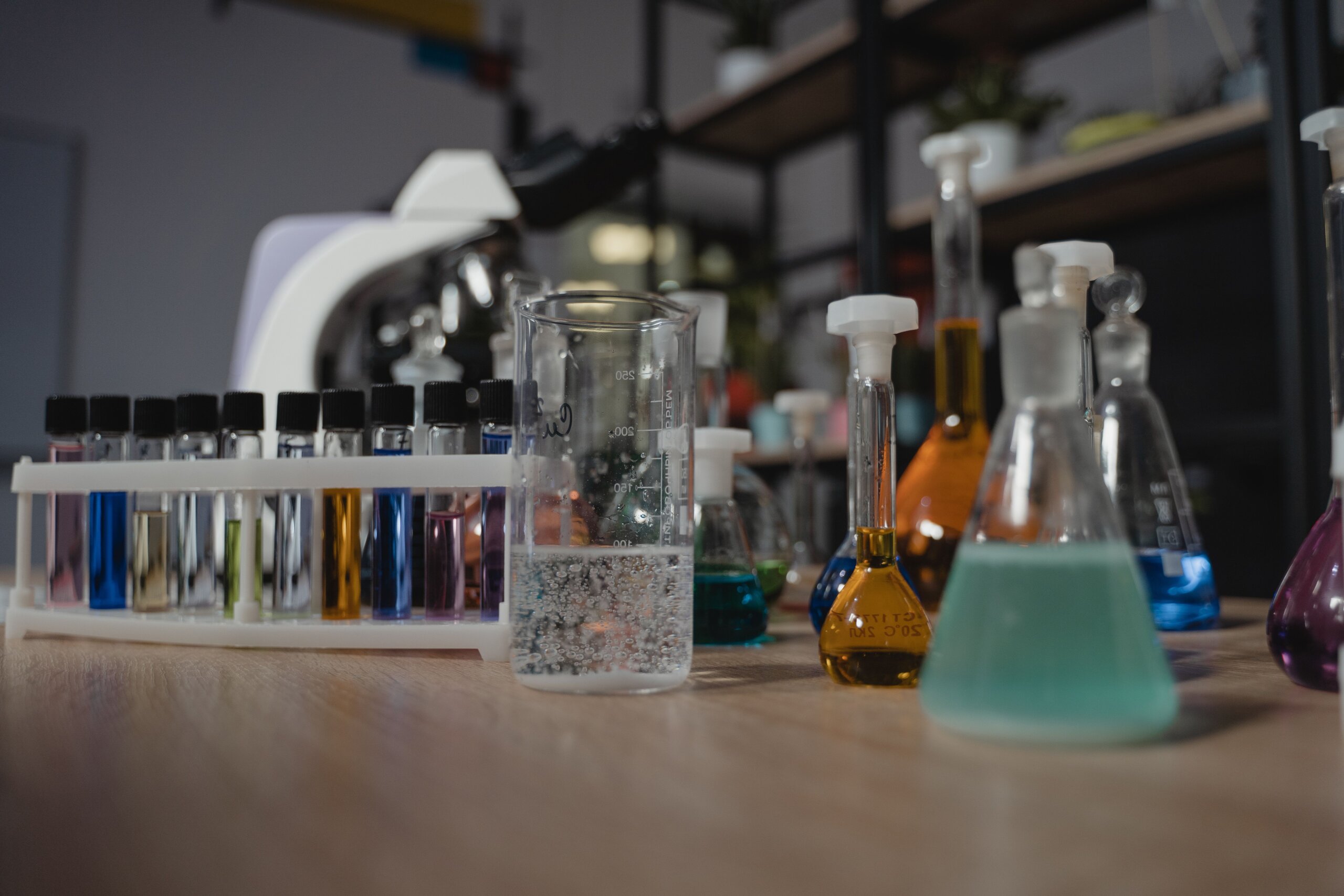 Glassware with colored liquids in a laboratory on a wooden table, showcasing diverse chemical research tools.